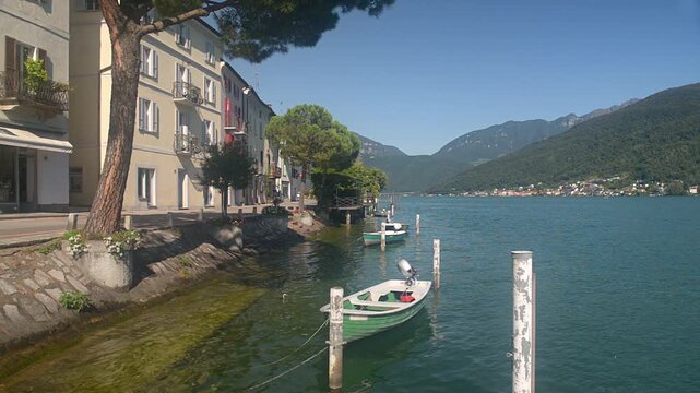 Lake Lugano in Morcote, Switzerland. Houses and a road just steps from the water, with small boats moored. Summer view, street Riveta da la Tor