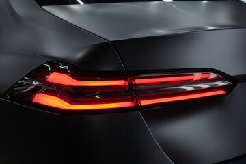 LED turn signal in the rear brake light of the car. Modern car lantern, close-up. Detail on the rear light of a black matte car. Close-up of a modern black sedan automobile with LED red taillights.
