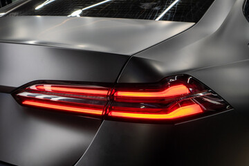 LED turn signal in the rear brake light of the car. Modern car lantern, close-up. Detail on the rear light of a black matte car. Close-up of a modern black sedan automobile with LED red taillights.