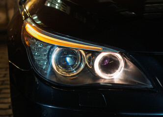 BI-LED headlights of a modern and expensive black car, hood and radiator grille. Front BI-LED headlight on a black SUV car. Glossy black premium car BI-LED headlights close-up. Angel eyes headlight. 