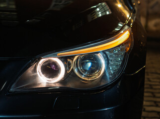 BI-LED headlights of a modern and expensive black car, hood and radiator grille. Front BI-LED headlight on a black SUV car. Glossy black premium car BI-LED headlights close-up. Angel eyes headlight. 