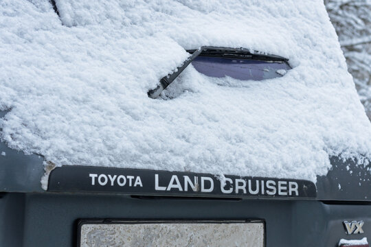 Toyota logo covered with snow. A gray Toyota Land Cruiser covered with snow is parked on the street. Snow-covered Land Cruiser 80 (J80) logo on the trunk lid in winter. Japanese SUV car. 