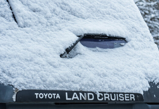 Toyota logo covered with snow. A gray Toyota Land Cruiser covered with snow is parked on the street. Snow-covered Land Cruiser 80 (J80) logo on the trunk lid in winter. Japanese SUV car. 