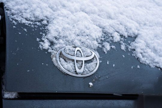 Toyota logo covered with snow. A gray Toyota Land Cruiser covered with snow is parked on the street. Snow-covered Land Cruiser 80 (J80) logo on the trunk lid in winter. Japanese SUV car. 