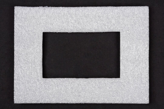 A rectangular frame made of white expanded polyethylene foam insulation material is centered against a dark black surface