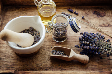 Making cold infused lavender olive oil. Olive oil, dried lavender blossoms puds in a glass jar. A mortar and pestle, along with a bundle of lavender flowers for decoration on rustic wood background.