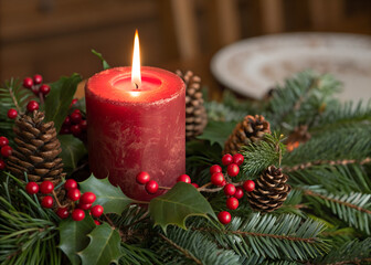 A festive Christmas wreath with a burning red candle and gold ornaments creates a shiny holiday decor featuring pine and holly for a warm winter advent celebration