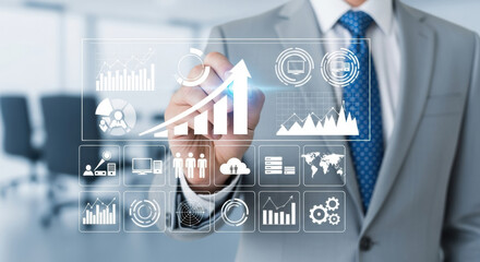 Close up of a businessman in a gray suit drawing a growth arrow on a transparent screen with various business graphs displaying data. Visuals include financial metrics and strategic planning elements.