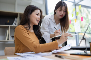 Fototapeta premium Two asian businesswoman using digital tablet and talking about business with analyzing financial charts in the modern office.