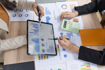 Two asian businesswoman using digital tablet and talking about business with analyzing financial charts in the modern office.