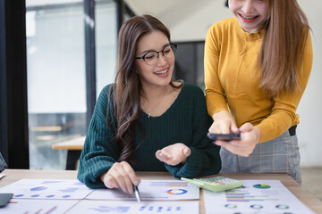 Fototapeta premium Two asian businesswoman using calculator and talking about business with analyzing financial charts in the modern office.