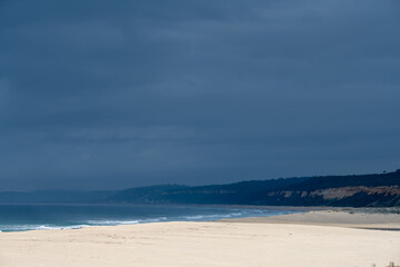 Fototapeta premium Empty Atlantic beach with distant cliffs under storm sky