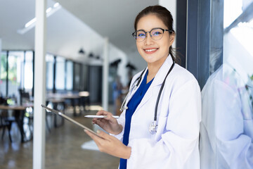 Doctor woman using digital tablet standing in clinic look at camera, Doctor woman wearing glasses and medical coat working in hospital, Healthcare professional service at modern center. 