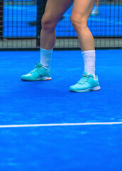 Close-up of the feet of a female padel player wearing turquoise shoes on a blue indoor padel court