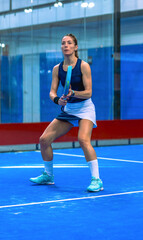 Professional female padel player in ready position holding racket on a blue indoor court