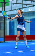 Athletic padel player completing a backhand stroke  with great extension and technique during an intense padel match on an indoor court.
