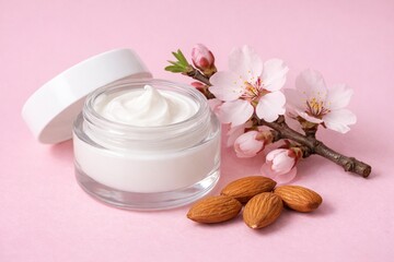 Glass jar of cream with white lid, surrounded by sprig of blossoming and almonds on pink background. Beauty product in transparent container. Cream butter moisturizing with almond oil