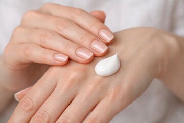 Woman is applying lotion to hands. Concept of self-care and relaxation, as woman takes time to pamper herself. Drop of cream positioned in middle of her palm