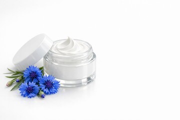 Glass jar of cream with white lid, near blue flowers. Beauty product. Remedy for face or skin around eyes with cornflower extract. Banner with copy space to advertise cosmetics white background