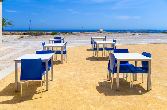 Tables and chairs of street restaurant outdoor cafe on empty square of Tabarca Island town and water of Mediterranean Sea Alicante bay on horizon in sunny summer day, Alicante province, Spain