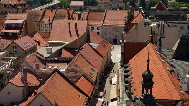 Maribor, Slovenia - August 9, 2025: An aerial view looks over the dense, terracotta-tiled roofs of Maribor's historic center toward distant rolling hills under a bright, clear blue sky.