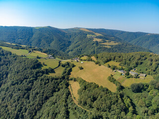 Aerial view of small villages connected by roads high up in a mountain landscape surrounded by pine forests and green meadows