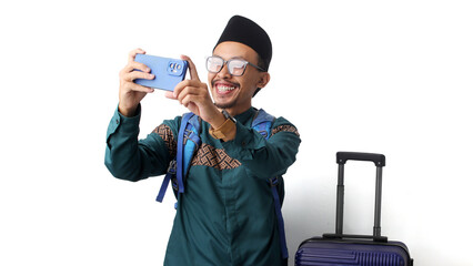 Asian Muslim man wearing a backpack, taking a selfie before departing for mudik, the Indonesian tradition of returning to one’s hometown to celebrate Eid Mubarak. Isolated on a white background.