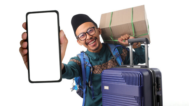 Happy Asian Muslim man holding a mobile phone with a blank white screen for mockup, while carrying a cardboard box and suitcase, going home for Eid Mubarak (mudik), Isolated on a white background.