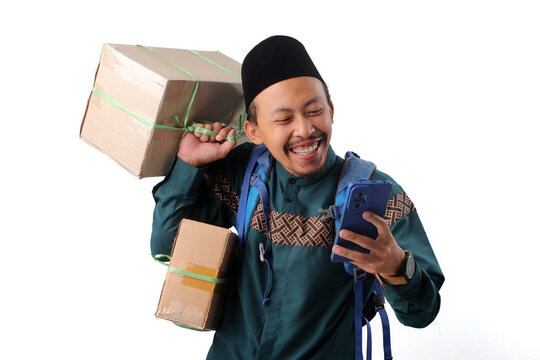 Asian Muslim man wearing a backpack and carrying boxes, smiling at his phone, ready for mudik to celebrate Eid Mubarak at his hometown, Isolated on a white background
