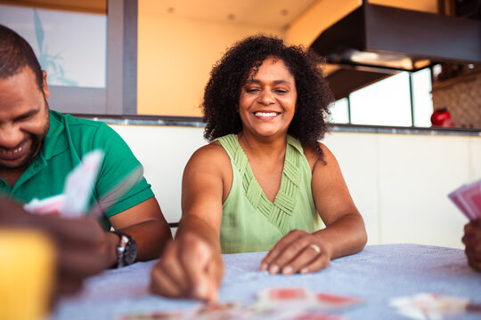Smiling middle-aged Black woman playing cards with friends, enjoying leisure time and social interaction.