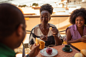 Smiling senior Black woman enjoys an outdoor breakfast with her family, sharing a happy moment together.
