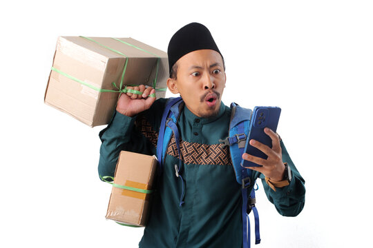 Shocked Asian Muslim man wearing a backpack, looking at his phone with a surprised expression after receiving unexpected traffic news during mudik for Eid Mubarak, Isolated on a white background