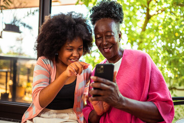 Happy African American grandmother and granddaughter sharing a joyful moment while looking at a smartphone together outdoors.