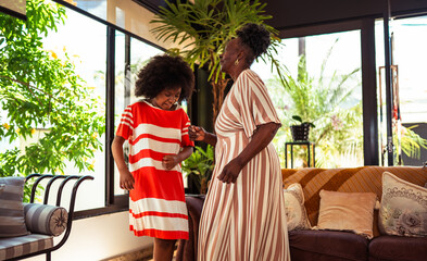 Happy African American grandmother and granddaughter dancing joyfully in a bright living room, celebrating their special bond.