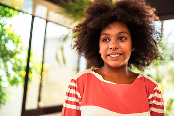 Smiling young Black woman with natural afro hair looks thoughtfully to the side in a bright room...