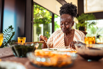Contented senior African American woman enjoying a healthy meal at home, savoring her food with a peaceful expression at the dining table.