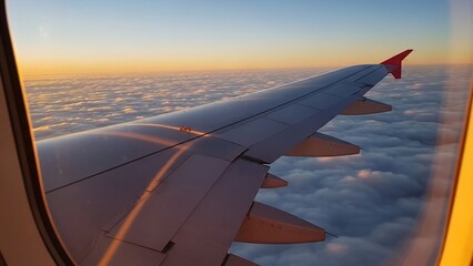 Panoramic view of an airplane wing flying above a magnificent cloudscape at golden hour.