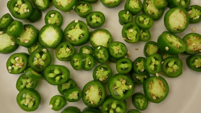 Green Jalapeno peppers slices on plate rotation top view.