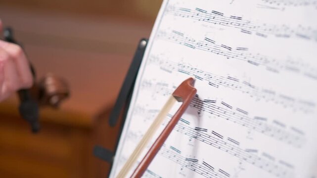 teacher studying sheet music closely, focused music instructor examining sheet music with annotations and bow, asian music teacher reviewing detailed sheet music with annotations and bow