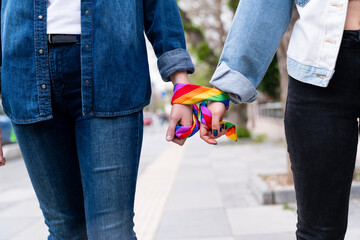 Two people holding hands, wearing rainbow-patterned scarves. The scarf is a symbol of the rainbow pride movement, representing love and acceptance for the LGBTQ community.