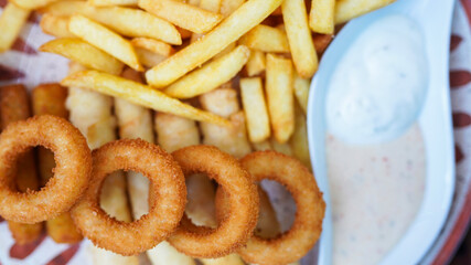 Plate of fried food with sauce. French fries, fried onion rings, and sauce.