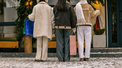 Three friends with shopping bags enjoying winter retail therapy outside a store