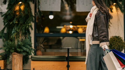 Woman with shopping bags walking past a cafe decorated with festive greenery and lights