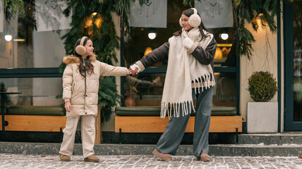 Mother and daughter holding hands walking in winter outside a cafe decorated with Christmas greenery