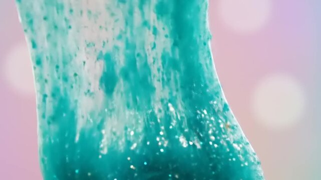 Stretching and dripping glittery turquoise slime in slow motion for satisfying sensory experience