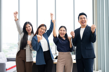 Group of happy Asian business people raising arms and celebrating success in office. Teamwork, victory, corporate achievement, and professional win concept with diverse colleagues