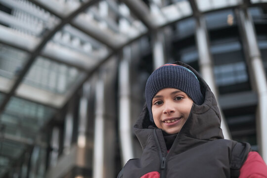 Ten Year Old Caucasian Boy Smiling at Camera Wearing Winter Hat with Building in the City