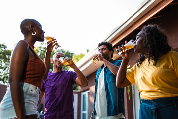 A diverse group of happy friends and family drink beer together at an outdoor backyard party.