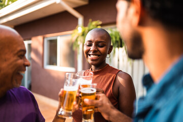 Happy multi-generational Black family or friends toasting with beer glasses during a backyard barbecue party at sunset.