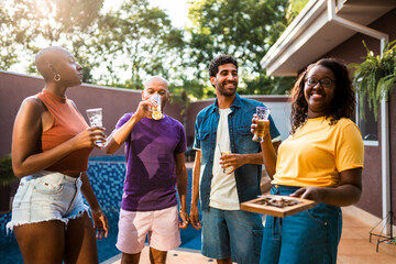 Diverse group of happy friends enjoying a backyard pool party with beer and snacks on a sunny...